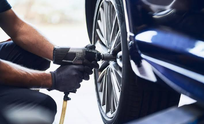 Mechanic using pneumatic impact wrench to tighten wheel on vehicle
